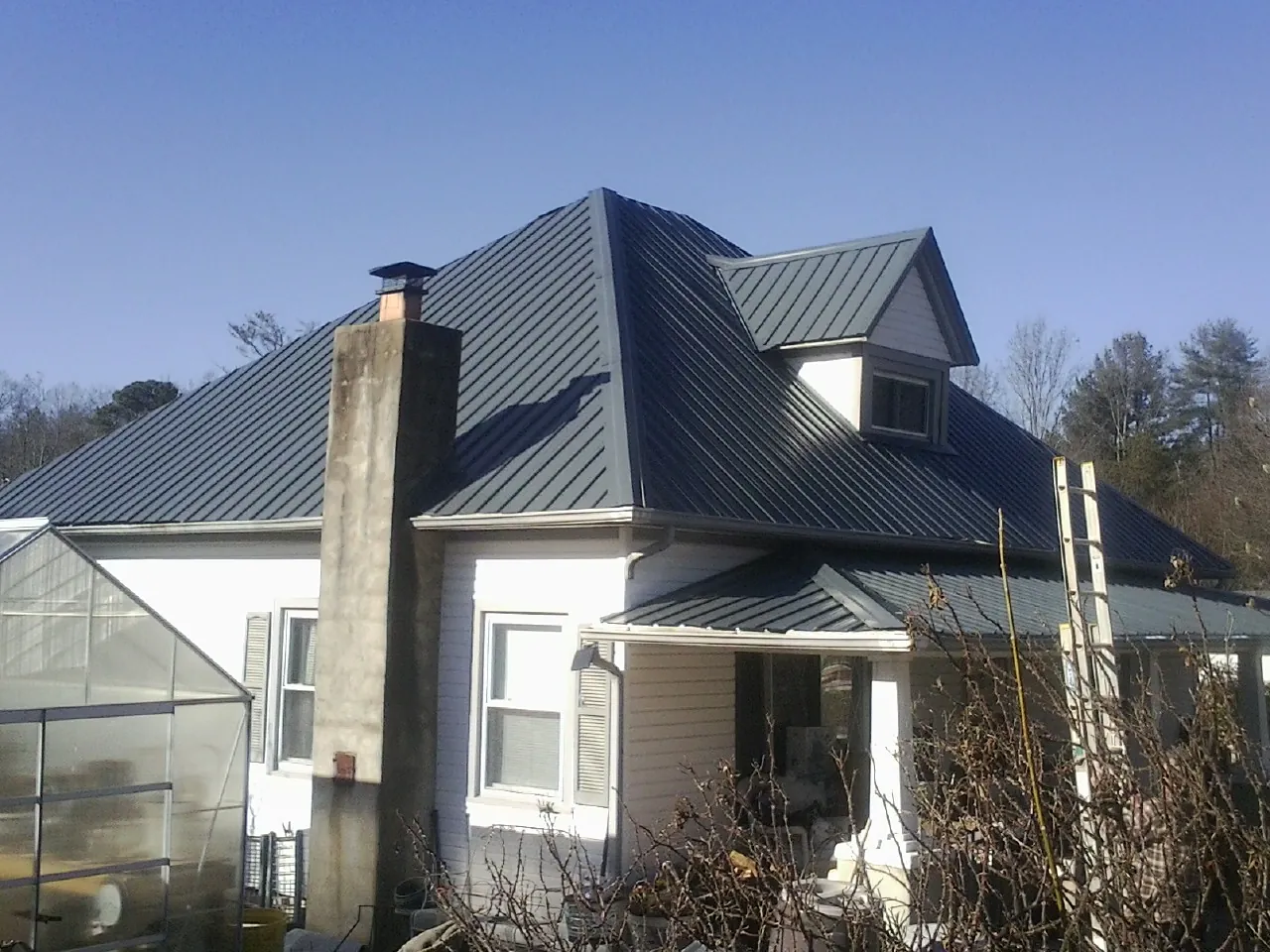 Dark blue standing seam metal roof on a white farmhouse with dormer — Slate & Tile Roof Repair by Roofing Brothers in Luckey