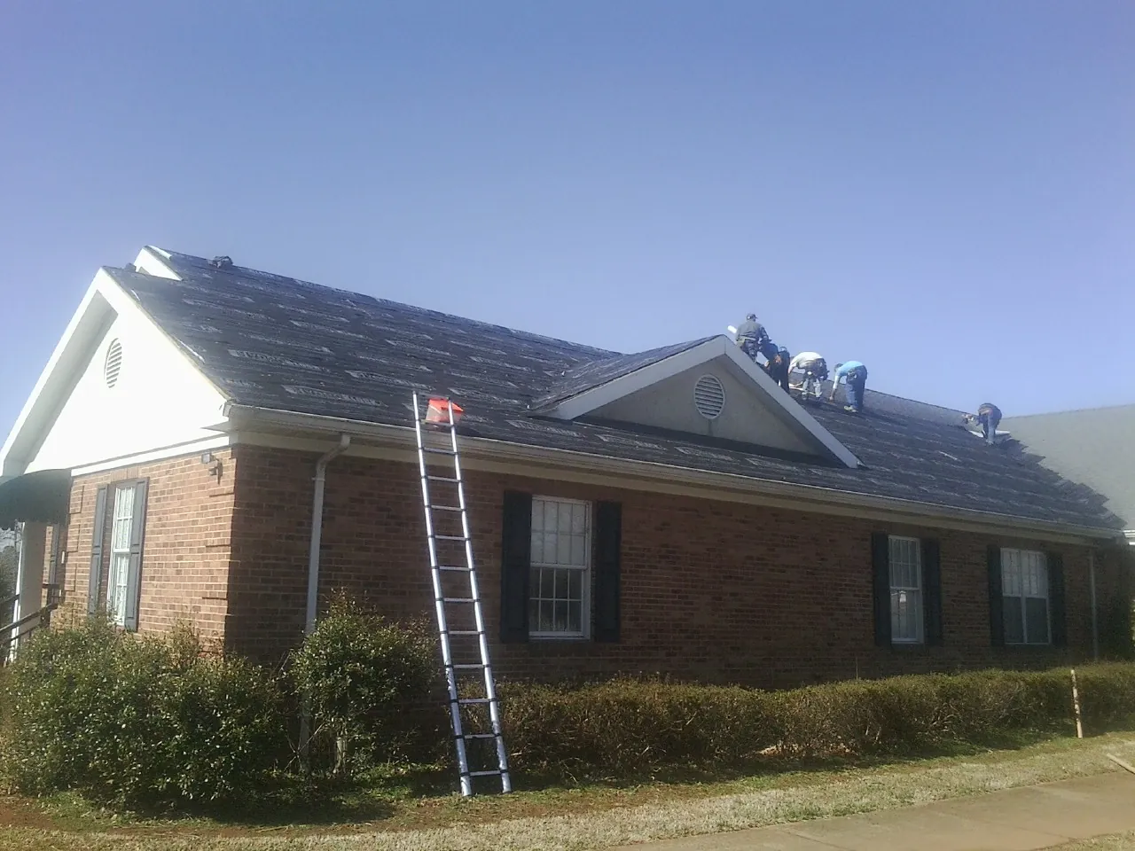 Crew tearing shingles off a brick ranch roof with a ladder set — Emergency Roof Repair work by our crew in Luckey