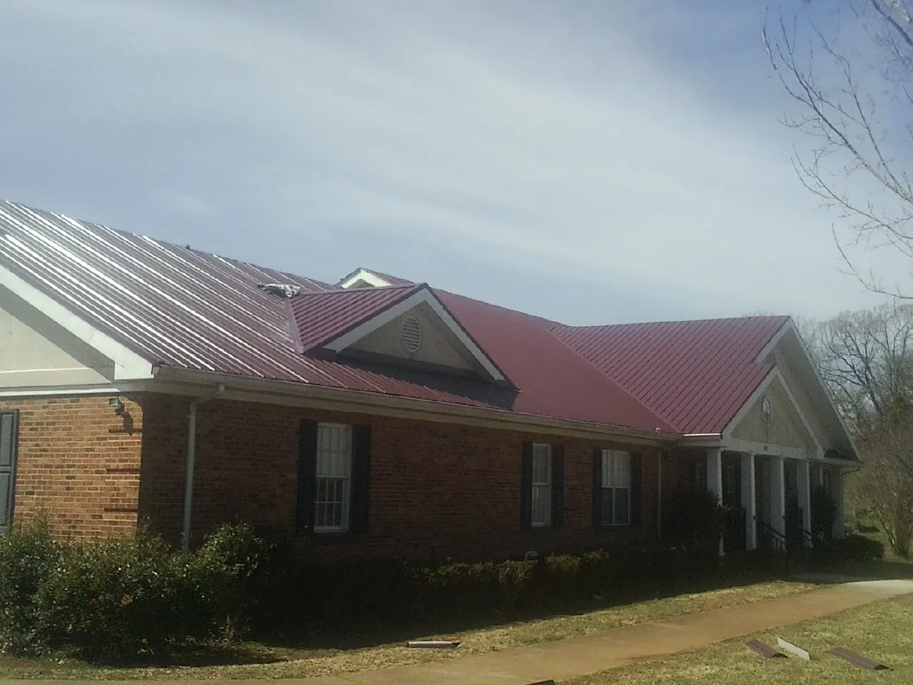 Red metal roof with gabled entries on a long brick building, from a Hail Damage Roof Repair job in Luckey