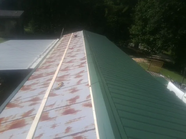 Old rusted panels beside newly installed green metal roofing — Wind Damage Roof Repair by Roofing Brothers in Luckey