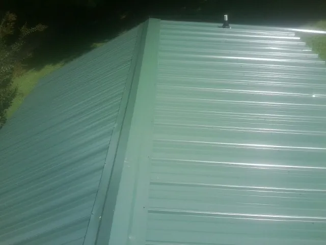 New green metal panels meeting at the ridge of a roof — Flat Roof Repair work by our crew in Luckey