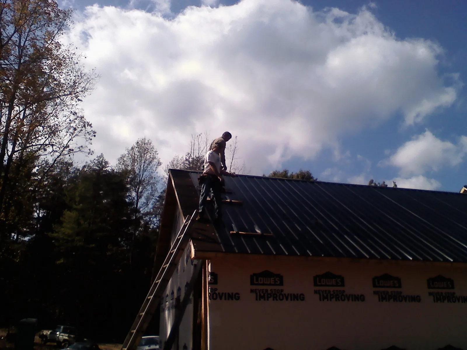 Roofer fastening dark metal panels high against a cloudy sky, from a Roof Inspection job in Luckey