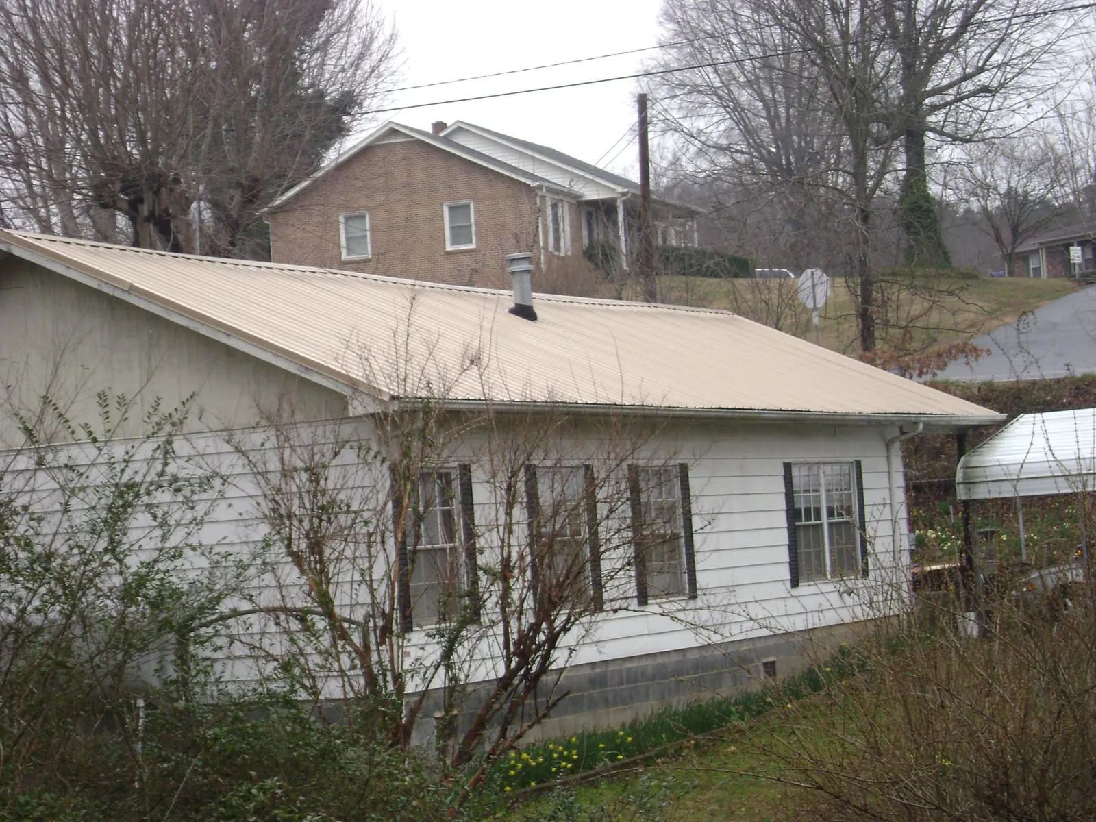 Tan metal roof on a white sided house set into a hillside — Commercial Roofing by Roofing Brothers in Luckey