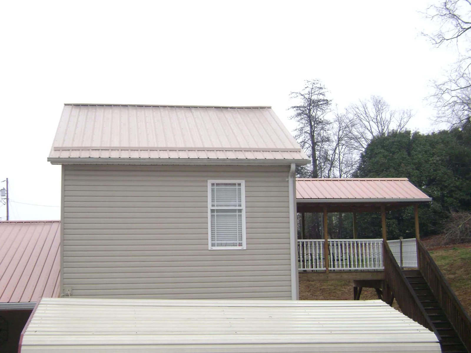 Tan metal roofs on a two story addition and attached porch, from a Roof Replacement job in Luckey